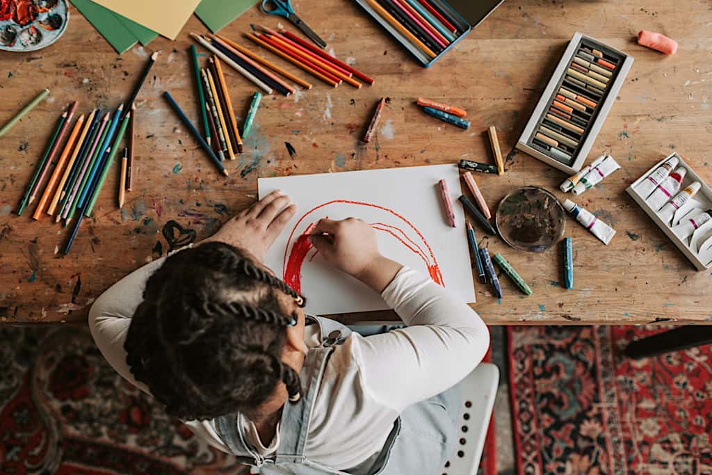 Vis et Deviens - un enfant dessinant sur une feuille blanche avec plusieurs feutres autour d'elle.